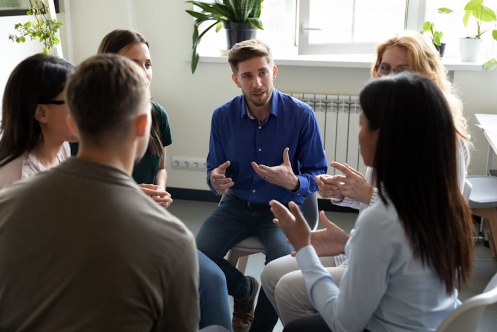 Man explaining concept in seated AA group meeting in rec room