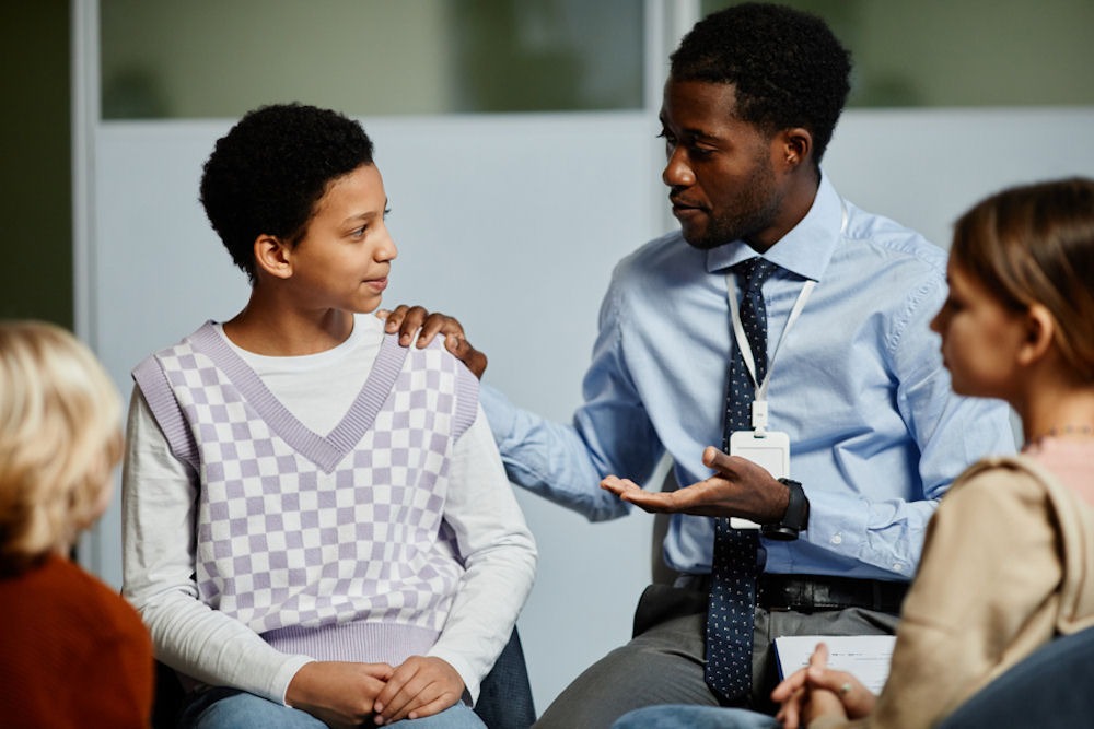 Children in a group therapy setting being encouraged by adult male mental health professional