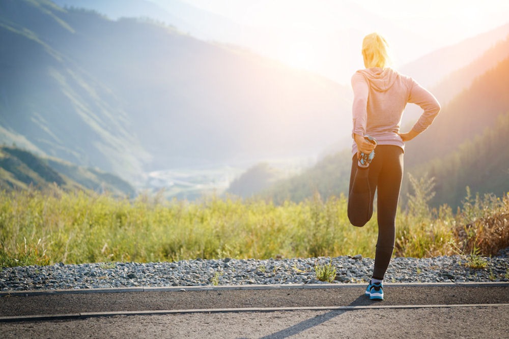 Woman runner on road, bending leg at the knee in standing stretch