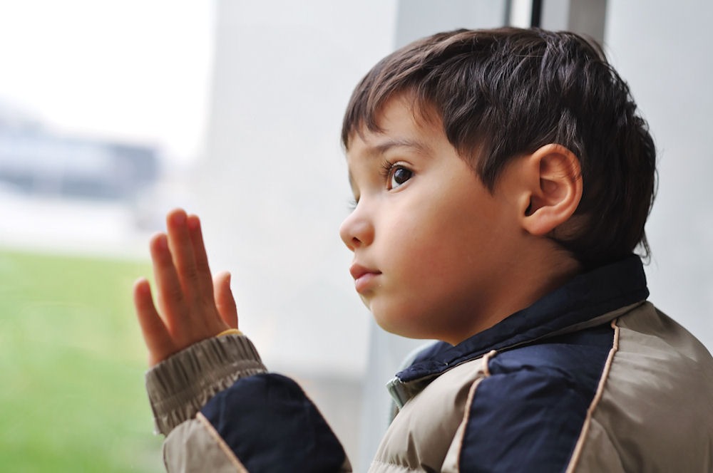 Young child in puffy winter coat looking wistfully out a window