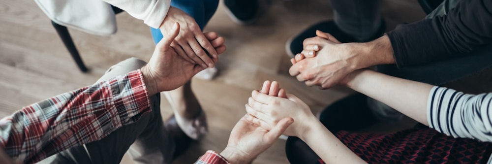 Overhead, faceless shot of four people in a circle holding hands