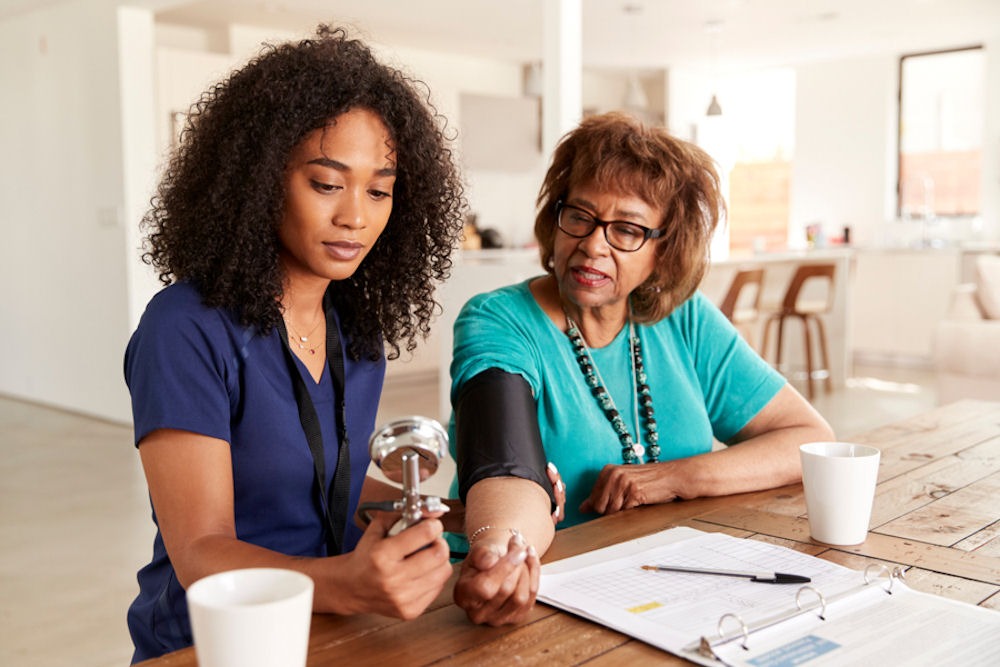 Older woman has blood pressure taken via cuff by medical professional in blue scrubs