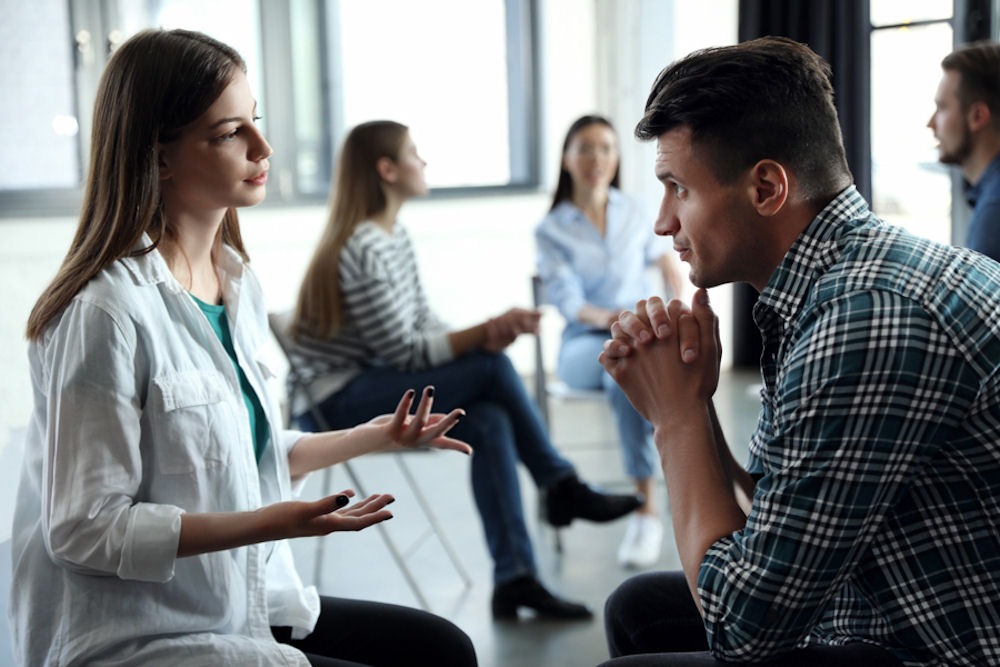 alcohol-addiction Man listening to woman speaking across from him in alcohol addiction support group